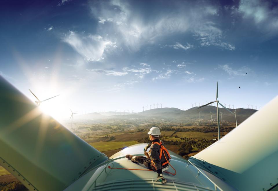 A man sitting on a wind turbine looking out over mountains