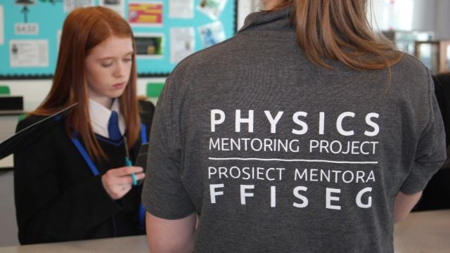 2 female students - one wearing school uniform and the other wearing a polo short saying Physics Mentoring Project