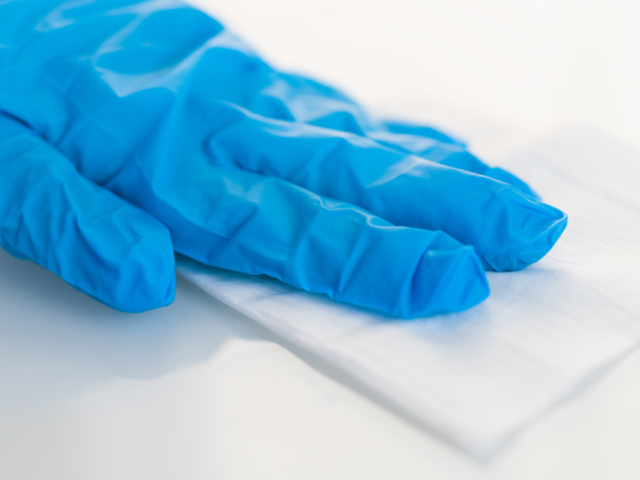 A hand in blue glove using a wipe on a white surface